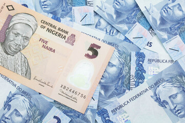 A close up image of a peach colored, five Nigerian naira bank note on a background of Brazilian two reais bank notes