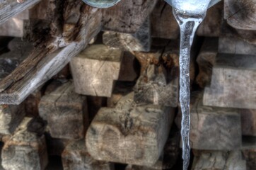 melting icicle hanging in front of wooden pole stack