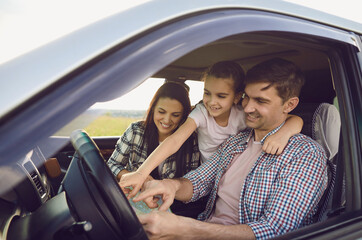 Happy young family looking on map in car salon on road trip. Loving parents with daughter traveling together by auto