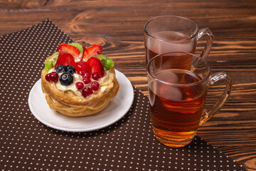 Home made cake with cream and fruit and hot tea on wooden table.