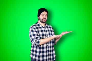 Fototapeta premium Young man pointing and looking at copy space. Handsome young businessman isolated on green background