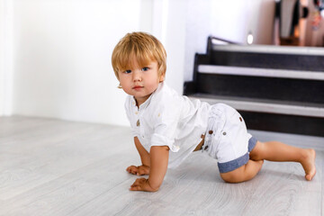 A beautiful healthy child crawls on the floor and looks at the camera with a smile. Happy little boy at home. Copy space for text