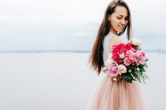 Bride with a bouquet of peonies on a lake background. Summer wedding bouquet. Wedding photo shoot of a brunette.