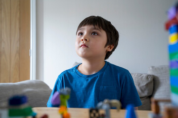 Portrait kid sitting on sofa looking up watching TV, Child with deep in thought while watching...
