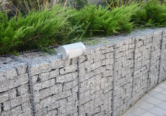 Retaining wall design: modern gabion wire mesh wall fence full with stones and outdoor lightning...