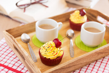 Cupcakes with whipped cream decorated with a cherry with cups of coffee made without lactose