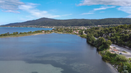 Mediterranean Greek landscape coastal drone shot. Aerial day top view of Sithonia Chalkidiki peninsula above shoreline with green plantation & low-rise houses by the sea.