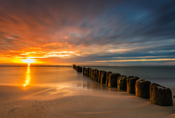 beautiful sunset on the Baltic Sea, waves washing the old wooden breakwaters