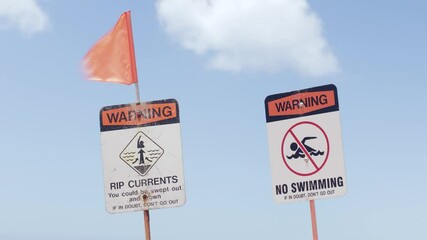 Rip current, no swimming beach warning signs, red flag blowing in wind. Close up, real time.