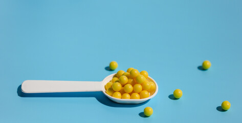 A white spoon filled with yellow vitamin C tablets on a blue background. Prevention of colds and flu