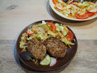 Fried buckwheat burgers and salad with cabbage, tomatoes, radish, cucumber and herbs in a brown plate. Natural food from cereals and vegetables for vegetarian nutrition.