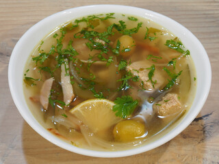 Isolated traditional Russian soup-meat Solyanka with pickles, sausages, lemon, olives, spicy herbs in a white bowl closeup, top view. Recipe for a delicious mixed of soup with vegetables