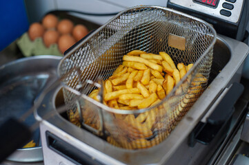 Top view of a deep fryer in which French fries are fried. Fresh finely chopped potatoes in a pan in hot oil
