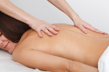 A close-up shot of a back massage. A young woman lies on her stomach on a white background. Masseuse hands stroking the client skin.