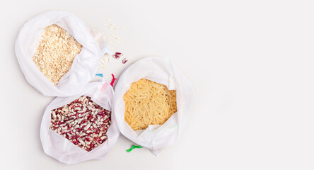 Eco friendly set reusable white bags on a light gray background with copy space. Red beans, pasta, organic oatmeal from the market. Waste-free shopping concept. ban plastic, zero waste