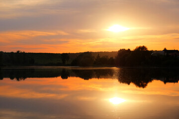 mellow sunset on countryside landscape with rural scenery reflection in pond water. Natural color of summer evening nature. Wide view
