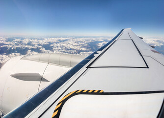 Clouds, mountains and sky seen through window of an aeroplane. Wing and engine of a modern fuel efficient twin-jet aircraft 