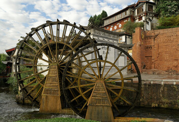 Fototapeta na wymiar Old wood water wheels turn on a rushing creek in the ancient Naxi town of Lijiang (Dayan), Yunnan Province, China.