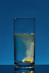 Close up of glass of water with effervescent aspirin tablet, pill in it isolated over blue background. Health concept