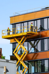 two workers on a scissor lift platform repair a building facade