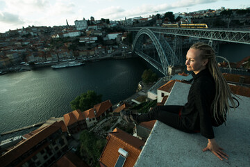 Tourist woman sitting in front of Douro river and Dom luis I bridge in the gloomy weather, Porto,...