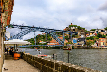 Outdoor restaurant terrace by Dom Luis I bridge in Ribeira and the Douro river with tourist boats in Porto, Portugal