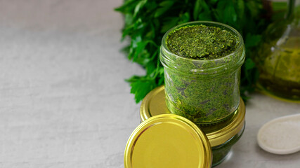 homemade pesto with cashew nuts in glass jar with mockup lug lid, green leaves of spicy herbs and olive oil on background. Vegan, healthy sauce, Italian cuisine. Horizontal banner with copy space.