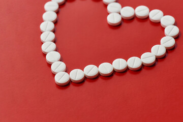 Heart made of white pills over red background. Heart and cardiovascular disease, health and treatment concept.