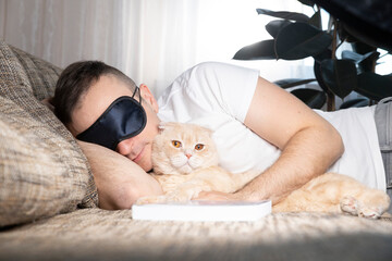 A young man falls asleep on a sofa with a book. Next to him is his beautiful ginger cat. The concept of rest and relaxation