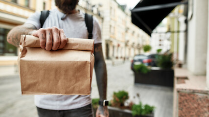 Cropped shot of delivery man holding paper bag while giving away order to a customer. Courier,...