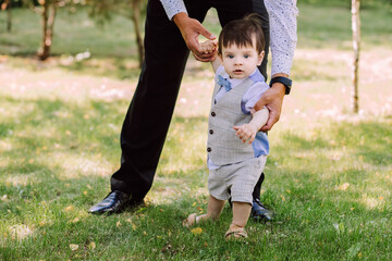 father teaches his little son to walk, family walks in the park, dad holds the child's hands and helps to walk, evening walk, father-son relationship, beautiful child