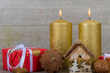 Christmas holidays composition with decorations (gold candles, pine cone and presents) on white wooden board background with copy space for your text.