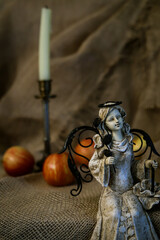 statuette of a sitting girl with wings on a background of red apples and candles in a candlestick close up