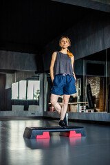 Young girl is doing fitness and different exercises in the gym.
Sport is health. Many sports equipment on  e background.
Themes of a healthy lifestyle.