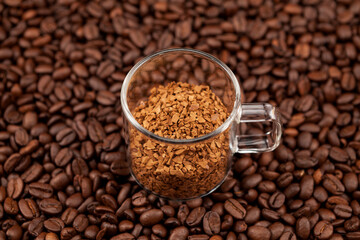 Instant, freeze-dried or granulated coffee in a transparent cup on the background of roasted coffee...