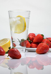Glass of water with ice and lemon on the background of strawberries