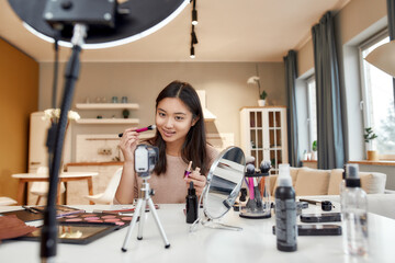 The Beauty Authority. Asian female blogger applying makeup while recording a tutorial video for her...