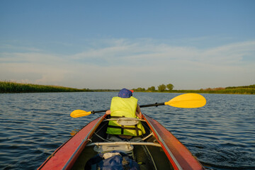 Obraz premium A little boy kayaks on the river in the summer and rowing an oar. The boy is floating in a boat on the river.