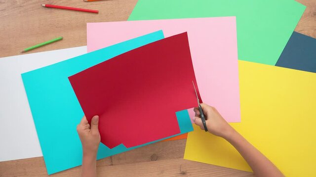 Child hands cutting colored paper with scissors. Top down view to table with colored paper. Learning, craft, art for children
