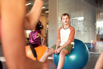 Teenage boy looking at female trainer while sitting on exercise ball in gym. Sport, healthy lifestyle, physical education concept © Svitlana