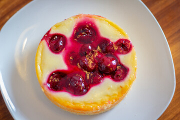 Cheesecake with cherry on a white plate on a wooden table.