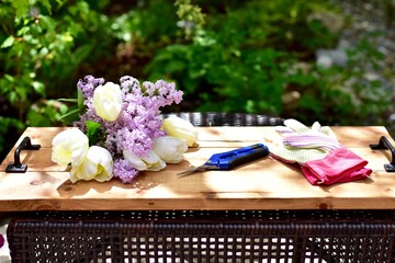 Outdoor garden setting with clippers and gardening gloves for cutting beautiful scented purple lilacs and gorgeous white tulips bouquet for thoughtful Mother's Day gift