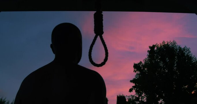 Man Trying to Commit Suicide by Hanging Himself on a Hangman Rope Changing his Mind and Leaving in Silhouette on a Sunset Sky Background a Concept New Life
