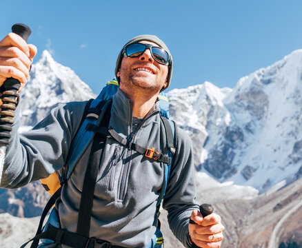 Portrait of smiling Hiker man on Taboche 6495m and Cholatse 6440m peaks background with trekking poles, UV protecting sunglasses. He enjoying mountain views during Everest Base Camp trekking route.
