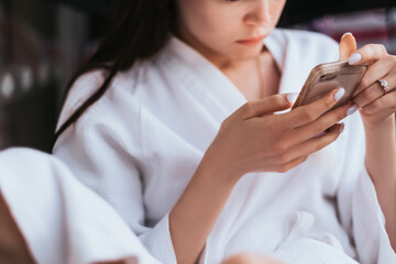 Woman in a white bathrobe in resort uses smartphone outdoor