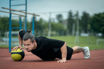 muscular young athlete has workout and exercising with medicine ball outdoor