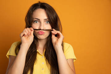 funny young woman who makes a mustache with a lock of her hair on an orange background