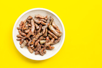 Turmeric root on pottery plate on yellow background.