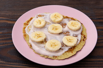 pancakes with yogurt lie on a plate with banana rings on a wooden background