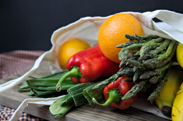 Cloth bag with usual fruits and vegetables on a table and dark background